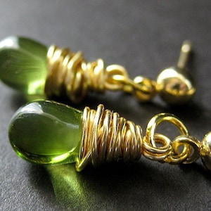 May include: A pair of gold earrings with green teardrop-shaped stones wrapped in gold wire. The earrings have a simple post back.
