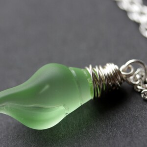 May include: A silver chain necklace with a green glass pendant wrapped in silver wire.