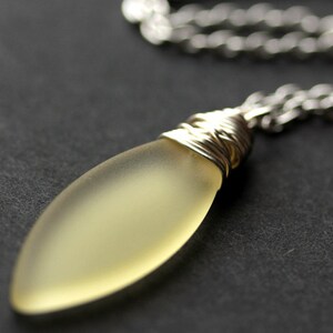 May include: A silver chain necklace with a frosted yellow glass pendant wrapped in silver wire.