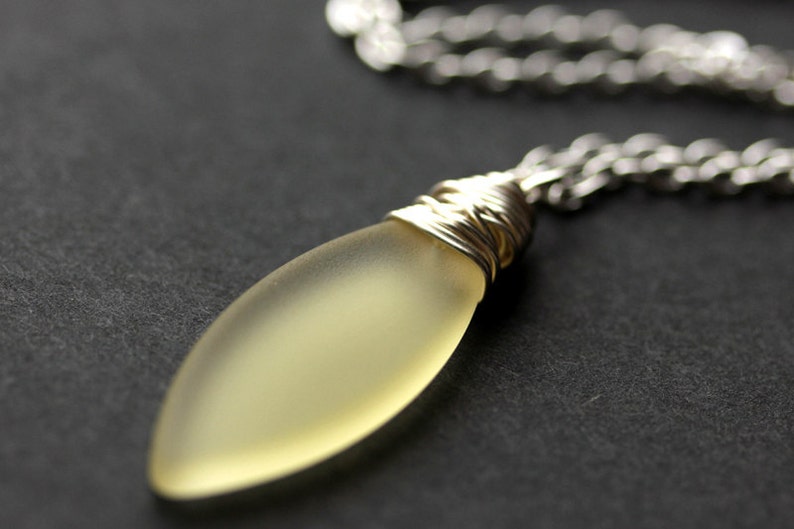 May include: A silver chain necklace with a frosted yellow glass pendant wrapped in silver wire.