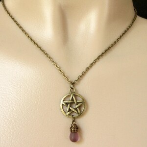 May include: A bronze chain necklace with a pentagram pendant and a purple glass bead.