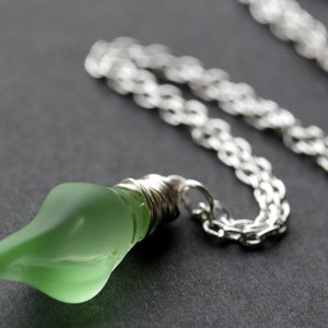 May include: A silver chain necklace with a green glass lightbulb pendant.