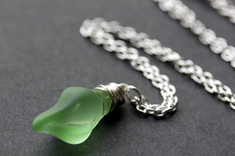 May include: A silver chain necklace with a green glass lightbulb pendant.