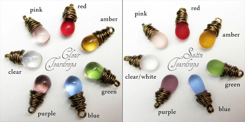 May include: Two rows of glass teardrop charms, each wrapped in wire. The top row features clear glass charms in colors like pink, red, amber, and clear. The bottom row features satin glass charms in colors like green, blue, purple, and clear/white.