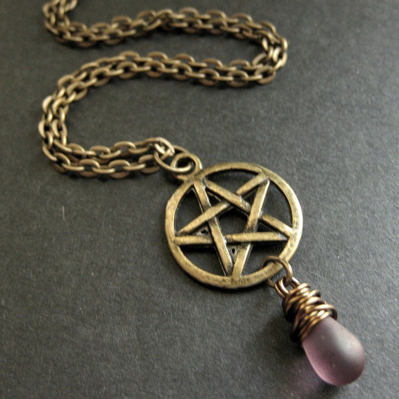 May include: A gold chain necklace with a pentagram pendant and a purple glass bead.