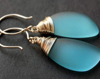 May include: A pair of silver wire wrapped earrings with frosted teal blue glass teardrop shaped pendants.