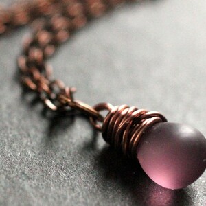 May include: A copper chain necklace with a purple glass bead wrapped in copper wire.