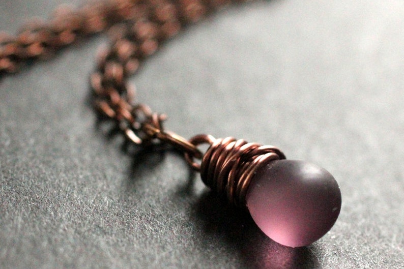 May include: A copper chain necklace with a purple glass bead wrapped in copper wire.