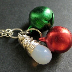 Puede incluir: Un collar de cadena de plata con tres dijes: una campana verde, una campana roja y una cuenta blanca.