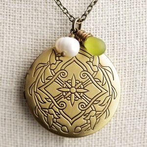 K&ouml;nnte beinhalten: Eine goldene Halskette mit einem detaillierten Blumenmuster. Das Medaillon hat eine wei&szlig;e Perle und eine gr&uuml;ne Glasperle daran.