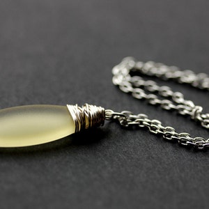 May include: A silver chain necklace with a light yellow glass pendant wrapped in silver wire.