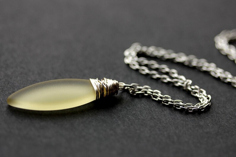 May include: A silver chain necklace with a light yellow glass pendant wrapped in silver wire.