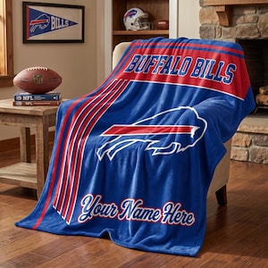 May include: A blue, red, and white fleece throw blanket featuring the Buffalo Bills logo, the text Buffalo Bills, and the customizable text Your Name Here in a script font, draped over a chair in a room with sports decor.