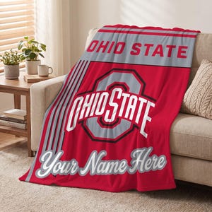 May include: A red, grey, and white fleece throw blanket featuring the Ohio State logo and text. The design includes the words OHIO STATE at the top, a large central Ohio State emblem, and the customizable text Your Name Here in script font.