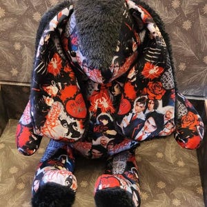 Könnte beinhalten: Ein Plüschhase mit einem Stoffmuster, das Bilder der Band My Chemical Romance, rote Rosen und den Text 'I'M NOT OKAY' zeigt. Der Hase hat lange Ohren, schwarze Kunstfellakzente an Ohren und Füßen sowie schwarze Knopfaugen.
