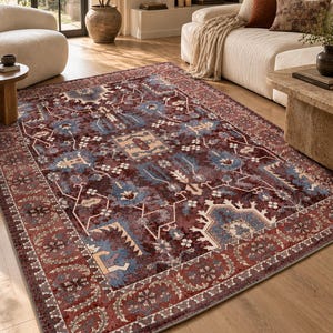 Peut inclure: Un tapis rectangulaire présentant une base rouge bordeaux profond avec des motifs complexes dans des tons bleu poussiéreux, crème et brun foncé. Le design comprend un médaillon central, des motifs floraux géométriques et une large bordure.