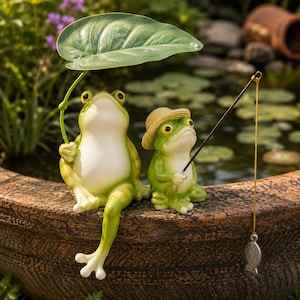 Può includere: Due statuette di rane verdi appollaiate sul bordo di una vasca marrone testurizzata. Una rana tiene una grande foglia verde sopra la testa come un ombrello, mentre la più piccola indossa un cappello di paglia e tiene una canna da pesca.