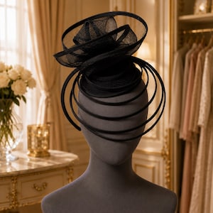 Peut inclure: Un bibi noir composé d'une base circulaire structurée avec une partie supérieure en maille transparente superposée et de multiples boucles en fil noir incurvées et concentriques descendant sur les côtés pour une silhouette architecturale.