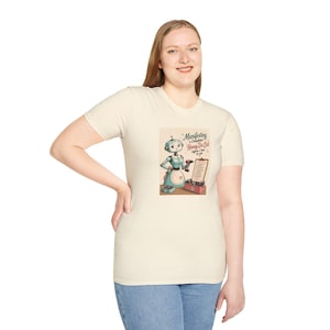 Könnte beinhalten: Ein cremefarbenes Kurzarm-T-Shirt mit einer Grafik eines Roboters im Retro-Stil, der eine Schürze trägt, eine Bohrmaschine hält und neben einem Klemmbrett mit dem Text "Manifesting a Completed Honey Do List before I had to ask." steht.