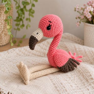 Op de afbeelding: Een handgemaakt gehaakt flamingo speelgoed met een felroze kop en lichaam, lange crèmekleurige poten met bijpassende voeten en donkerbruine vleugelpunten. De flamingo heeft een crèmekleurige snavel met een donkerbruine punt en zwarte veiligheidsogen.