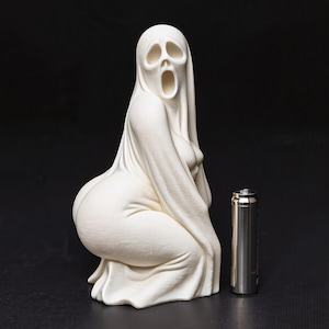 Könnte beinhalten: Eine mattweiße Geisterfigur mit schreiendem Gesichtsausdruck, gehüllt in ein fließendes, gewandartiges Kleidungsstück. Die Figur kniet. Eine silberne zylindrische Batterie steht daneben und dient als Referenz für die Größe.