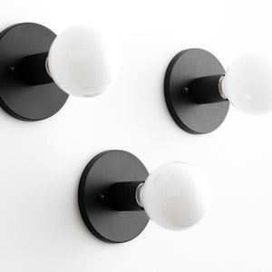 May include: Three black wall-mounted light fixtures with round white light bulbs.