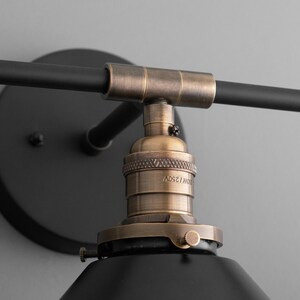 May include: Black and brass wall sconce with a black metal shade and a brass socket. The socket is labeled "E27 125V".