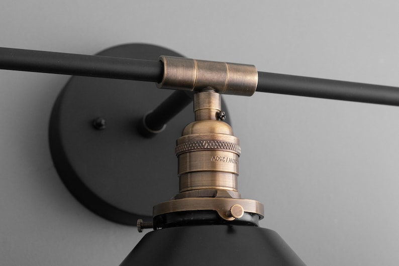 May include: Black and brass wall sconce with a black metal shade and a brass socket. The socket is labeled "E27 125V".