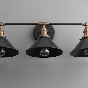 May include: A black three-light vanity light fixture with black metal shades and brass accents.