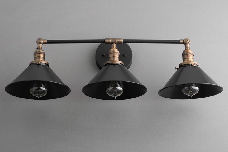 May include: A black three-light vanity light fixture with black metal shades and brass accents.