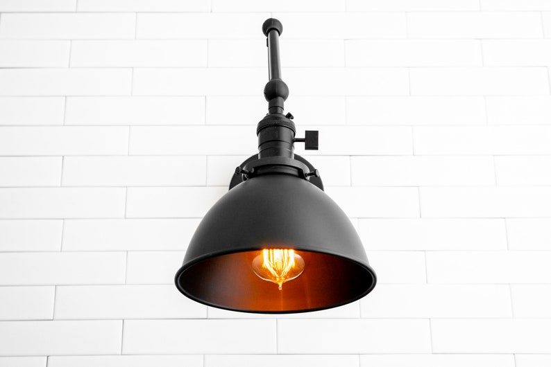 May include: Black metal wall sconce with a dome-shaped shade and an exposed bulb. The sconce is mounted on a white brick wall.