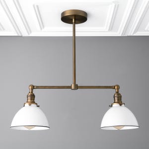 May include: A two-light pendant light fixture with a brass finish and white glass shades. The fixture has a straight rod with two arms extending out to the sides, each holding a white glass shade.