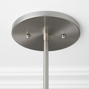 May include: Close-up of a brushed nickel ceiling mount for a pendant light fixture. The mount has two screws and a center hole for the hanging rod.