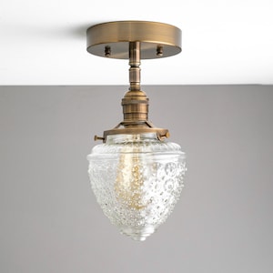 May include: A brass ceiling light fixture with a clear glass shade featuring a textured pattern. The shade is shaped like a bell and has a bulb inside.
