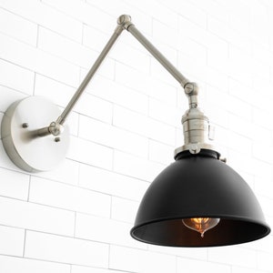 May include: A black metal wall sconce with a silver adjustable arm. The sconce has a black metal shade and a clear light bulb.