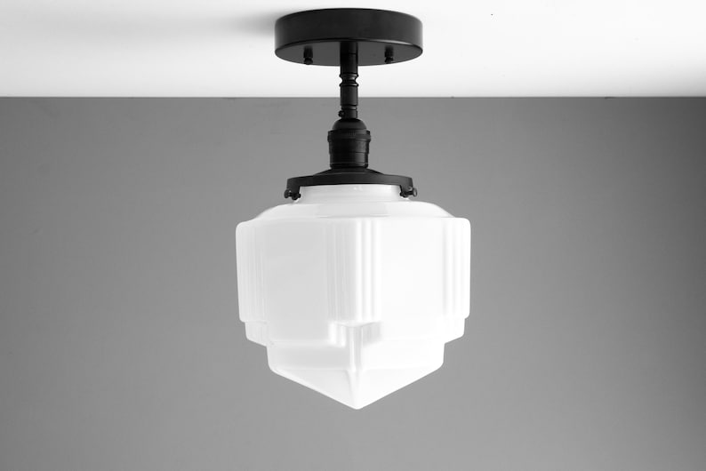 Puede incluir: Una l&aacute;mpara de techo de vidrio blanco con un dise&ntilde;o geom&eacute;trico. La l&aacute;mpara tiene una base de metal negro y una pantalla de vidrio blanco.