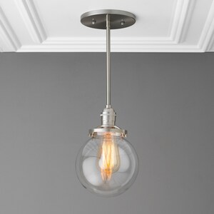 May include: A silver pendant light with a clear glass globe shade and a warm white light bulb.