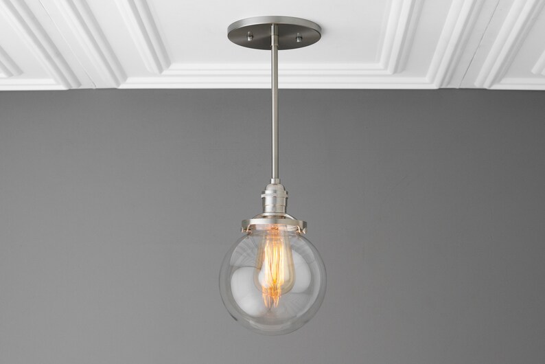 May include: A silver pendant light with a clear glass globe shade and a warm white light bulb.