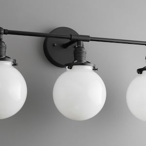 May include: Black three-light bathroom vanity fixture with globe-shaped frosted glass shades.