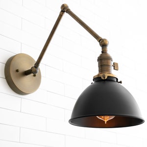 May include: A black metal wall sconce with a brass arm and base. The sconce has a round black shade and a clear light bulb.
