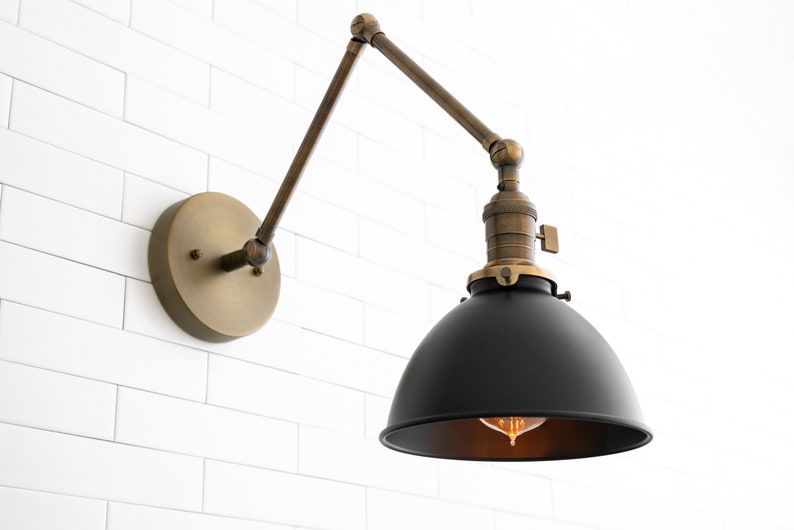 May include: A black metal wall sconce with a brass arm and base. The sconce has a round black shade and a clear light bulb.