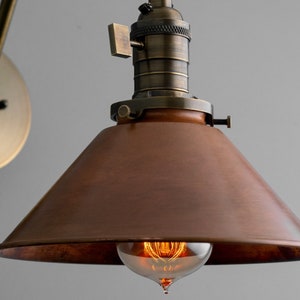 K&ouml;nnte beinhalten: Vintage Wandleuchte mit kupferfarbenem, konischem Schirm und messingfarbenem Arm und Montageplatte. Die Leuchte verf&uuml;gt &uuml;ber eine freiliegende Edison-Gl&uuml;hbirne, die ihre industrielle &Auml;sthetik unterstreicht. Der Schirm hat einen Durchmesser von ca. 20 cm.
