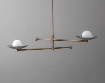 May include: A ceiling light fixture featuring a central vertical rod with two horizontal arms extending in opposite directions. Each arm holds a shallow, dark gray bowl-shaped shade topped with a spherical white glass light bulb at the end.