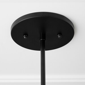 May include: Black ceiling mount for a pendant light fixture. The mount has two screws and a round, flat base.