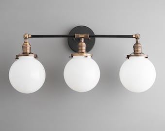 May include: A three-light vanity fixture with a black metal frame and three white glass globes. The fixture has a brushed brass finish.