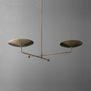 May include: A brass pendant light fixture with three circular shades and a long, thin rod connecting them.