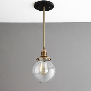 May include: A brass pendant light with a clear glass globe shade. The light fixture has a black ceiling mount.