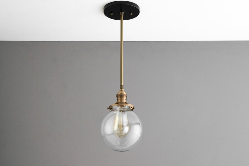 May include: A brass pendant light with a clear glass globe shade. The light fixture has a black ceiling mount.