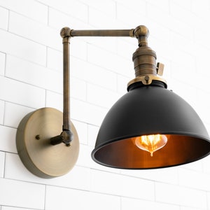 May include: A black metal wall sconce with a brass arm and base. The sconce has a dome-shaped shade and a vintage-style light bulb.