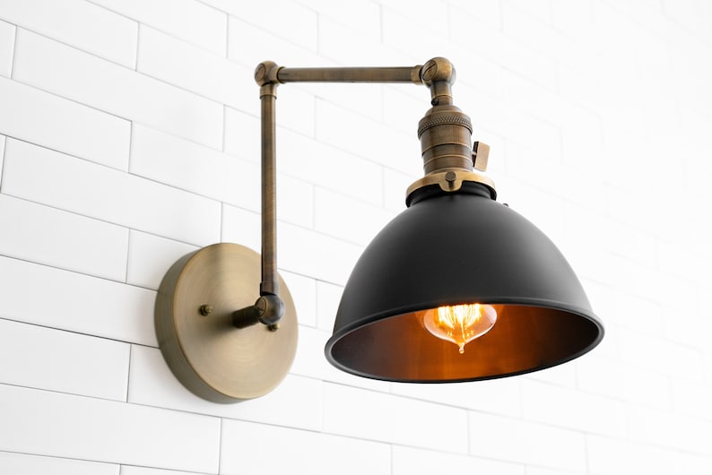 May include: A black metal wall sconce with a brass arm and base. The sconce has a dome-shaped shade and a vintage-style light bulb.